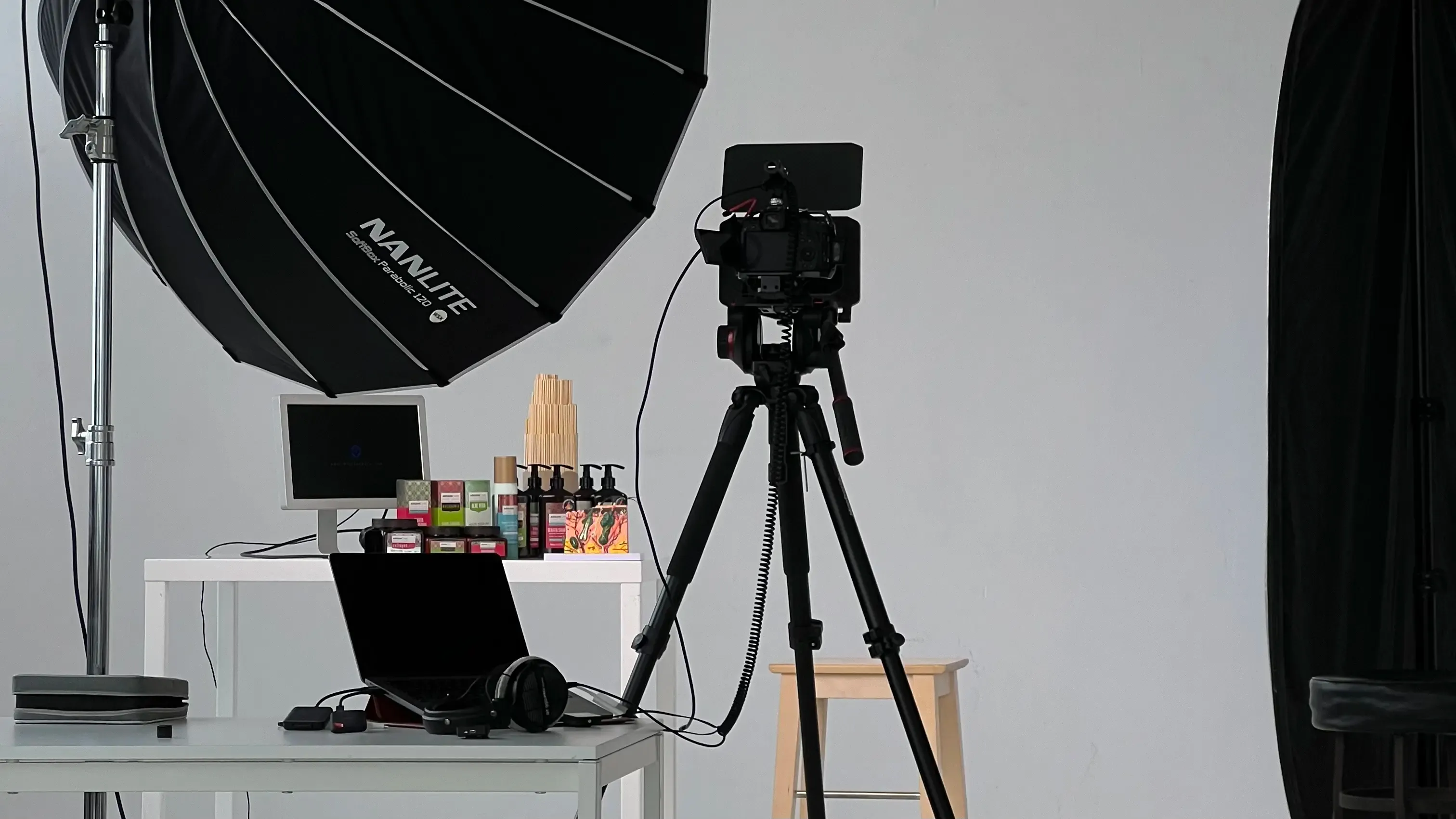 Plan zdjęciowy w studiu: kamera na statywie i softbox ustawione przed stołem z kosmetykami przygotowanym do sesji produktowej
